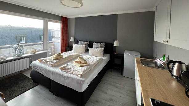 A modern hotel room with a large bed, a small kitchenette, a window with a view, and a ceiling light. - Strönwai - Perfect for sunbathing or enjoying the vacation life of the Strandstraße (Sylt)