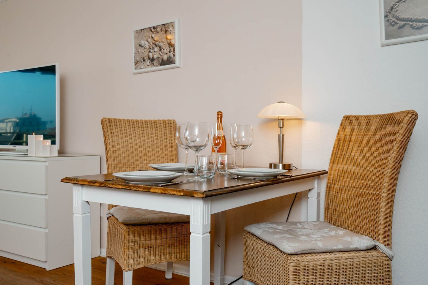 Ein Essbereich mit Tisch für zwei Personen, Korbstühle, einem Fernseher und einer Lampe.