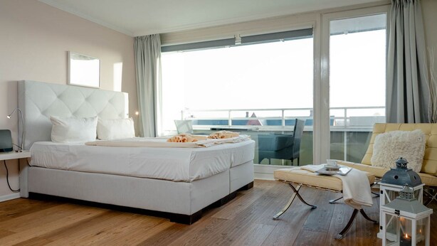 Una habitación de hotel moderna con una cama grande, un balcón con vistas y un área de descanso con una mesa y sillas.