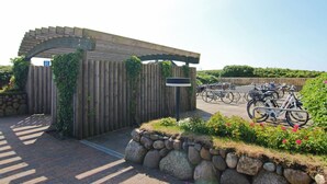 Ingresso con pergola in legno, un cartello, un muro in pietra e un'area dedicata al parcheggio biciclette con biciclette.