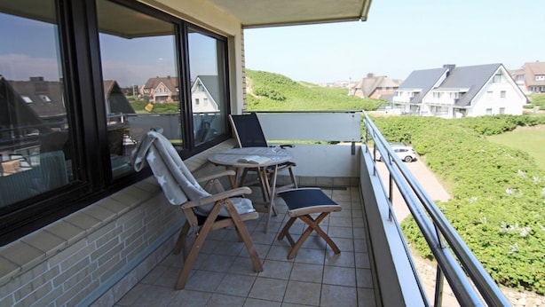 Un balcone con tavolo e sedie, affaccia su una zona residenziale con case e vegetazione.