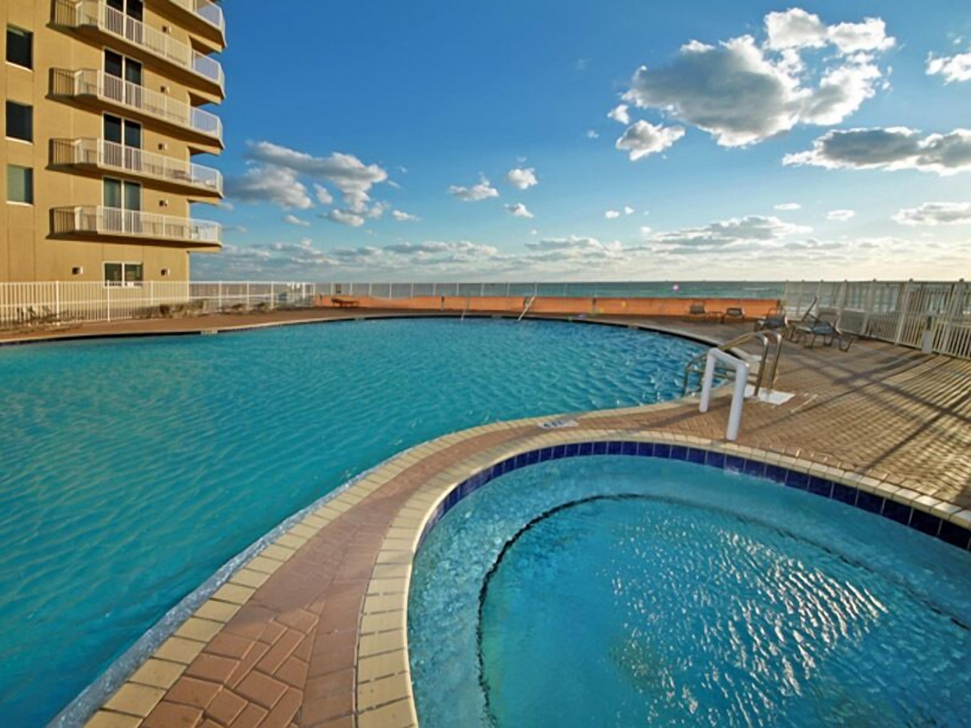 A swimming pool with a curved edge, a tiled deck, and a view of the ocean.