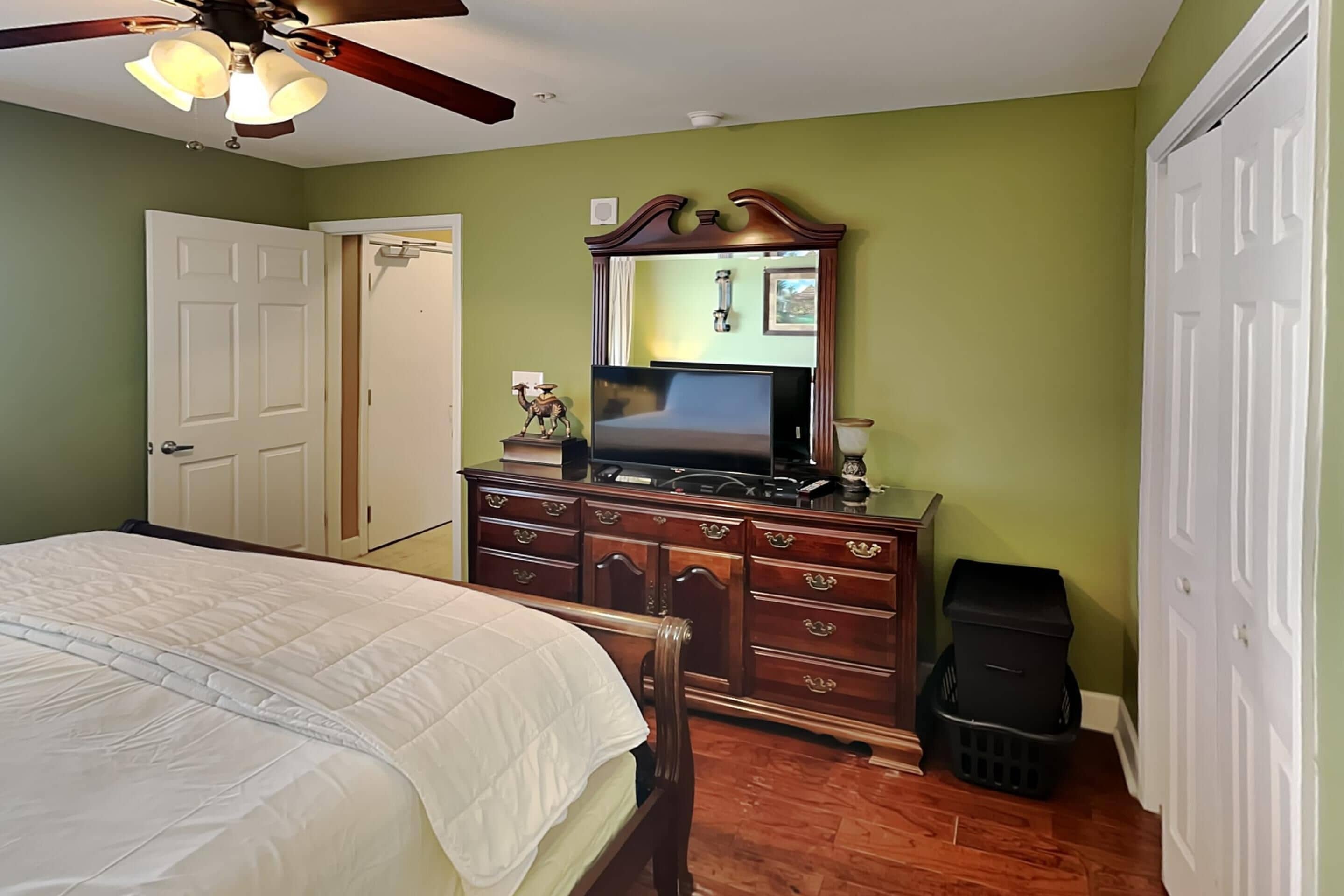 A bedroom with a bed, dresser, television, and a ceiling fan.