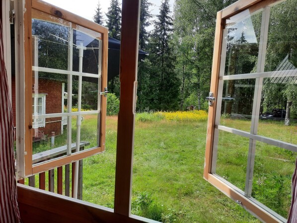 A view through open windows of a grassy yard with a wooden deck, a brick building, and a forested area. - Beautiful vacation property with secluded location in the forest (Nora)