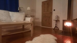 Een gezellige kamer met een bed, een houten tafel, een witte vachttapijt, een houten deur en een houtkachel.