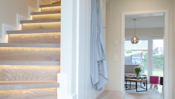A modern staircase with wooden steps and a bench, leading to a dining area with a table and chairs.