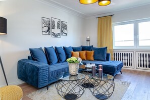A modern living room with a blue sectional sofa, a glass coffee table, and a yellow curtain. - Inge-Marie - Exclusive living pleasure - for relaxed vacation days for four (Sylt)