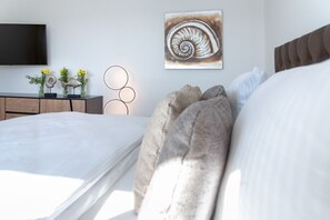 A modern bedroom with a large bed, a flat-screen TV, a wall-mounted artwork of a spiral shell, and a bedside table with decorative items. - Inge-Marie - Exclusive living pleasure - for relaxed vacation days for four (Sylt)