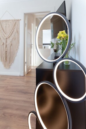 A modern interior with a black console, a round mirror with illuminated edges, and a macrame wall hanging. - Inge-Marie - Exclusive Lifestyle - For a Relaxing Vacation for Four (Sylt)