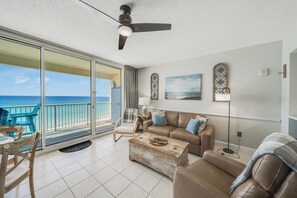 A living room with a balcony, a ceiling fan, a sofa, a coffee table, and a view of the ocean.
