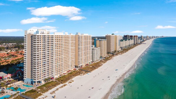 A beachfront hotel with multiple high-rise buildings, a sandy beach, and a clear blue ocean.