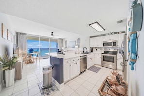 A modern kitchen with white cabinets, a central island, a view to the outside, and a balcony with outdoor furniture.