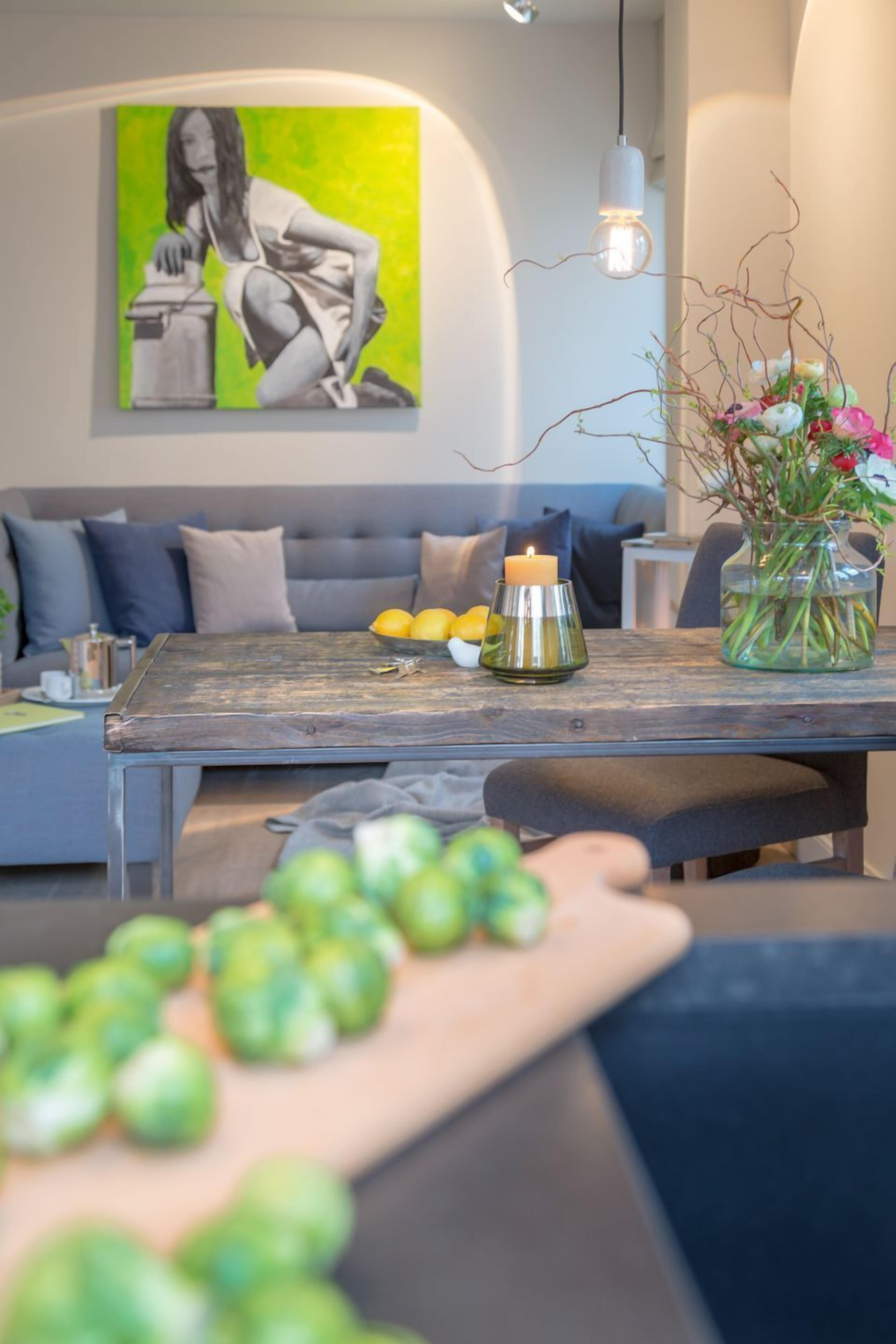 A modern living room with a sofa, a wooden coffee table, a vase with flowers, and a painting on the wall.