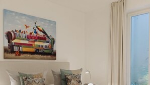 Een slaapkamer met een groot bed, een schilderij aan de muur en uitzicht op zee door een raam.