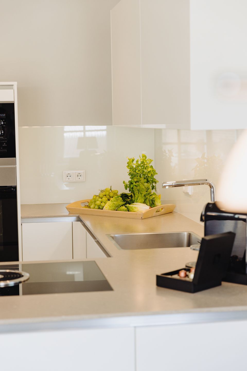 A modern kitchen with white cabinetry, a stainless steel sink, and a countertop with a fruit bowl and a small plant.