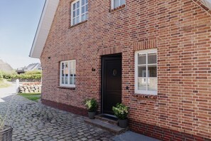 A brick house with a black door, two windows, and a stone pathway leading to the entrance.