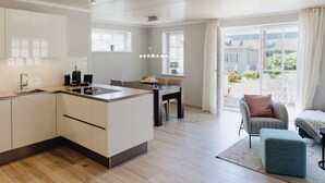 Een moderne keuken met een centraal eiland, een eetgedeelte met tafel en stoelen, en een gezellige zithoek met een fauteuil en poef.