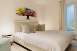 A bedroom with a large bed, a bedside table, a chair, and a window with curtains.