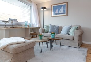 Ett modernt vardagsrum med en soffa, två sidobord, en golvlampa och en inramad tavla på väggen.