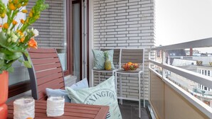 A balcony with a wooden table, two chairs, a small fruit bowl, and a potted plant.