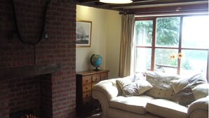 A cozy living room with a brick fireplace, a cream-colored sofa, and a window with a view of greenery.