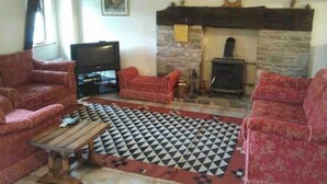A living room with two red sofas, a wooden coffee table, a black and white patterned rug, a television, and a stone fireplace.