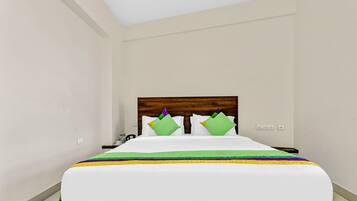 Een hotelkamer met een houten hoofdeinde, een bed met wit beddengoed, groene en gele kussens, en een nachtkastje met een lamp.