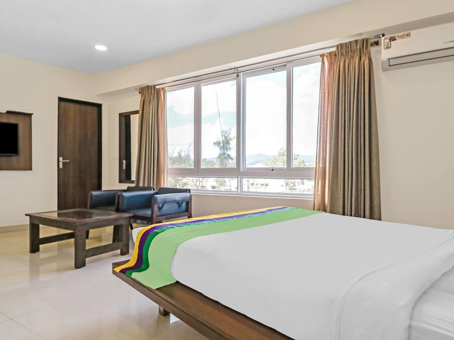 Habitación de hotel con cama, escritorio, silla, televisor y ventana con cortinas.