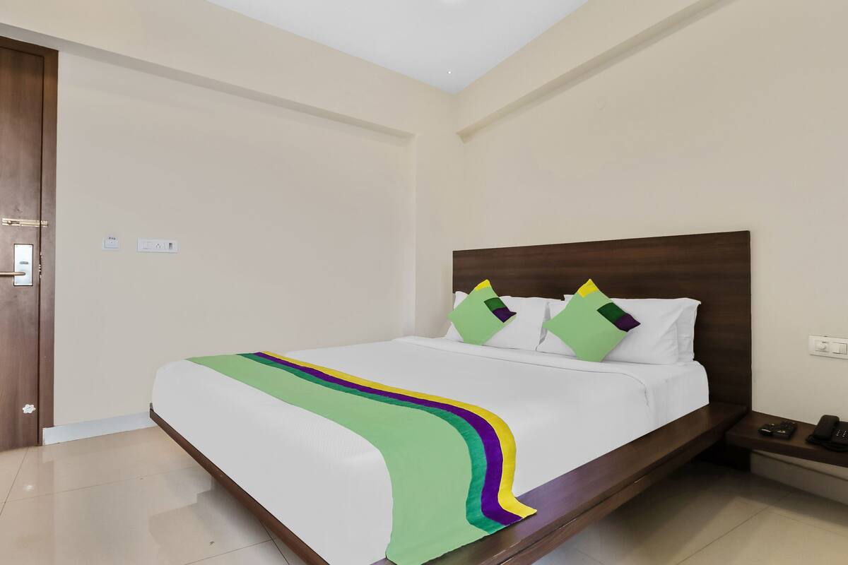 Uma cama bem arrumada com um cobertor colorido, uma cabeceira de madeira e uma mesa de cabeceira com um telefone e controle remoto.
