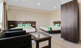 A hotel room with two beds, a glass-top table, and a dark-colored armchair.