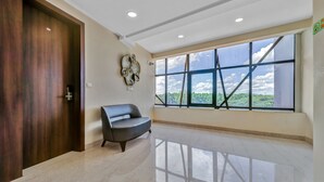A spacious room with a large window, a wooden door, and a modern chair. - Treebo Punarnava Bypass Road (Chikkamagaluru)