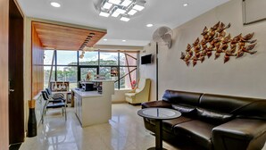 A modern hotel lobby with a leather sofa, a small round table, a reception desk, and a large window offering a view of the outdoors. - Treebo Punarnava Bypass Road (Chikkamagaluru)