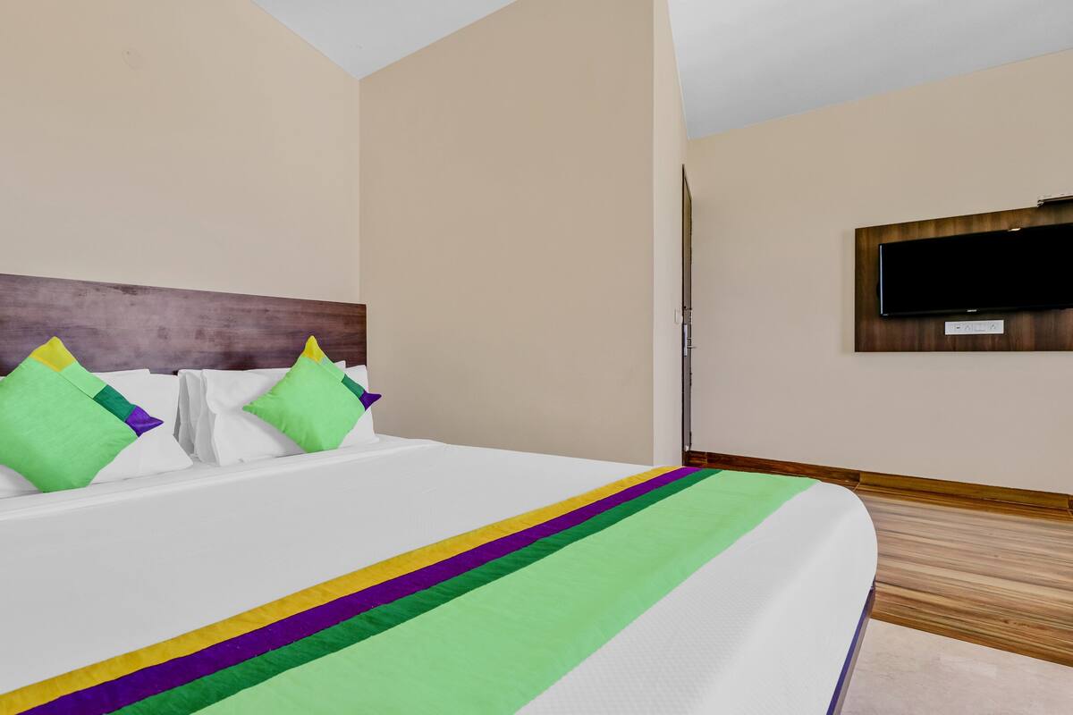 Quarto de hotel com uma cama grande, cabeceira de madeira, televisão de tela plana na parede e uma porta que dá para outro quarto.