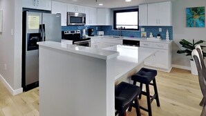 Une cuisine moderne avec des meubles blancs, des appareils en acier inoxydable et un îlot central doté de tabourets de bar.