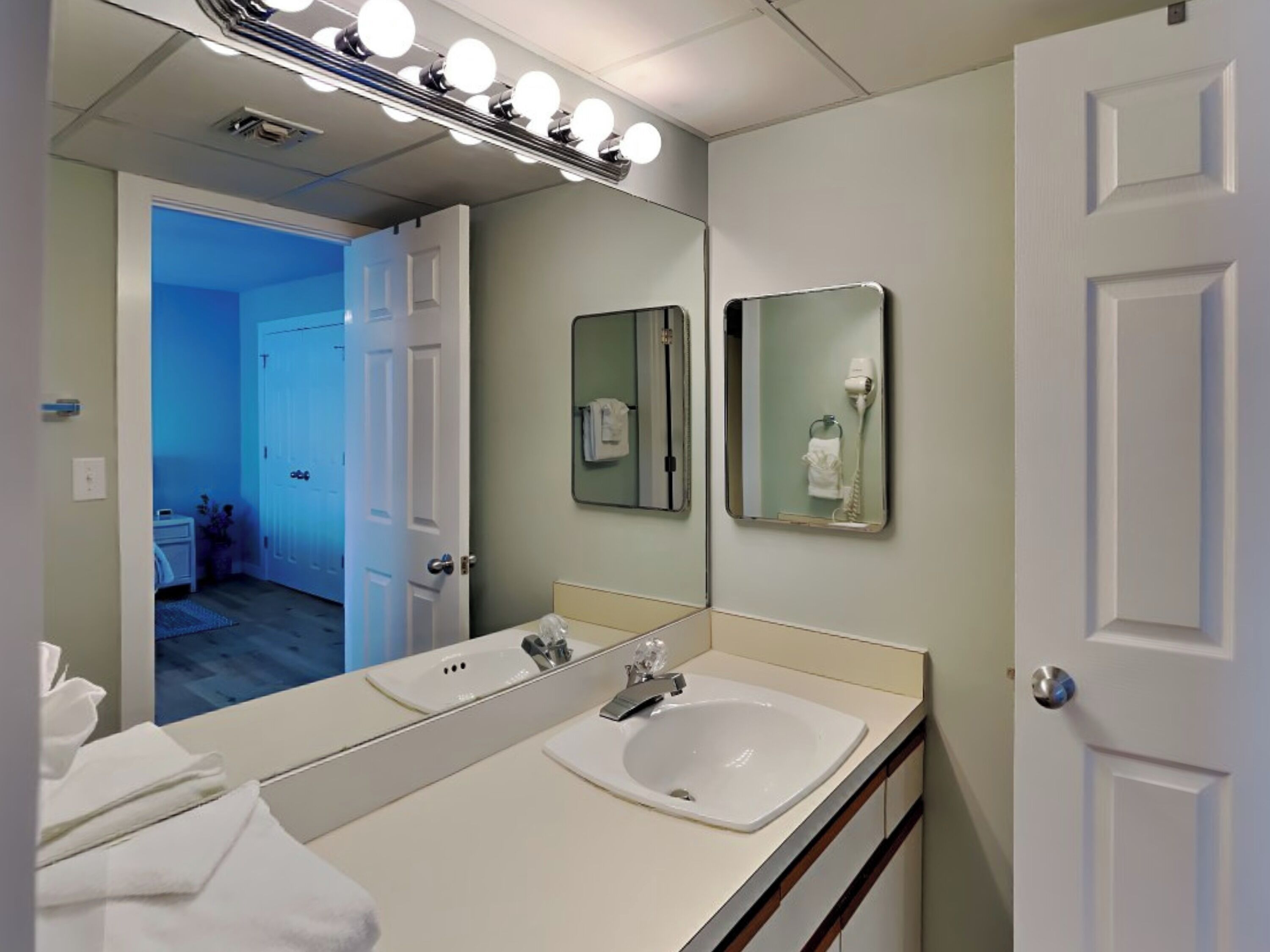 A bathroom with a large mirror, two sinks, and a hairdryer.