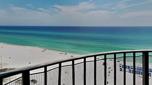 Une vue sur la plage depuis un balcon doté d’une balustrade, avec un ciel dégagé et une mer calme.