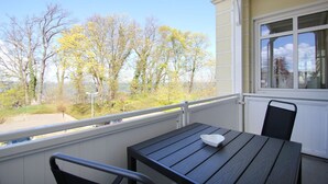 A balcony with a table and chairs, overlooking a park with trees and a body of water.