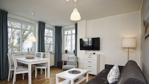 A modern living room with a dining area, a sofa, a TV, and a lamp.