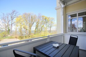 Ein Balkon mit Tisch und Stühlen, mit Blick auf einen Park mit Bäumen und einem Gewässer.