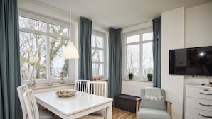 A modern kitchen with a dining area, large windows, a TV, and a cozy seating arrangement.