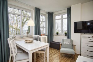 A modern kitchen with a dining area, large windows, a TV, and a cozy seating arrangement.