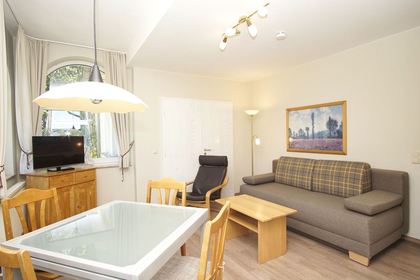 A modern living room with a glass-top dining table, a sofa, a TV, and a painting on the wall.