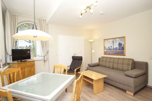 Ein modernes Wohnzimmer mit einem Esstisch mit Glasplatte, einer Couch, einem Fernseher und einem Bild an der Wand.