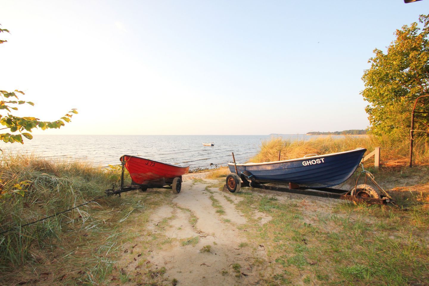 Zwei Boote, eines rot und eines blau, liegen auf einem Feldweg am Wasser.
