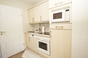 A compact kitchen with a microwave, oven, and sink. - Near the beach, with a balcony - Villa Strandmuschel FeWo 07 - Villa Strandmuschel (Göhren)