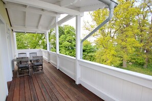 A covered porch with a wooden deck, white railings, and a table with chairs. - Close to the beach, with balcony - Villa Strandmuschel FeWo 08 - Villa Strandmuschel (Göhren)