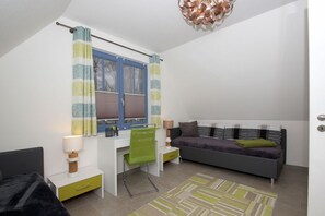 A compact bedroom with a bed, a desk with a chair, a sofa, and a window with curtains.