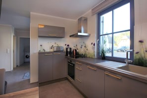 A modern kitchen with grey cabinets, a stainless steel range hood, a toaster, and a coffee maker. - Vacation home Stranddistel - close to the beach, thatched roof, with garden, sauna, dog-friendly (Glowe)