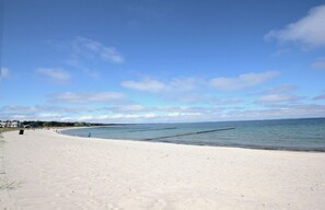 A wide sandy beach with calm waters, a clear sky, and a few buildings in the distance. - Vacation home Stranddistel - close to the beach, thatched roof, with garden, sauna, dog-friendly (Glowe)