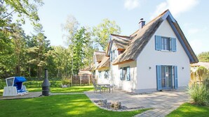 Ett hus med ett halmtak, vita väggar och blå fönsterluckor.